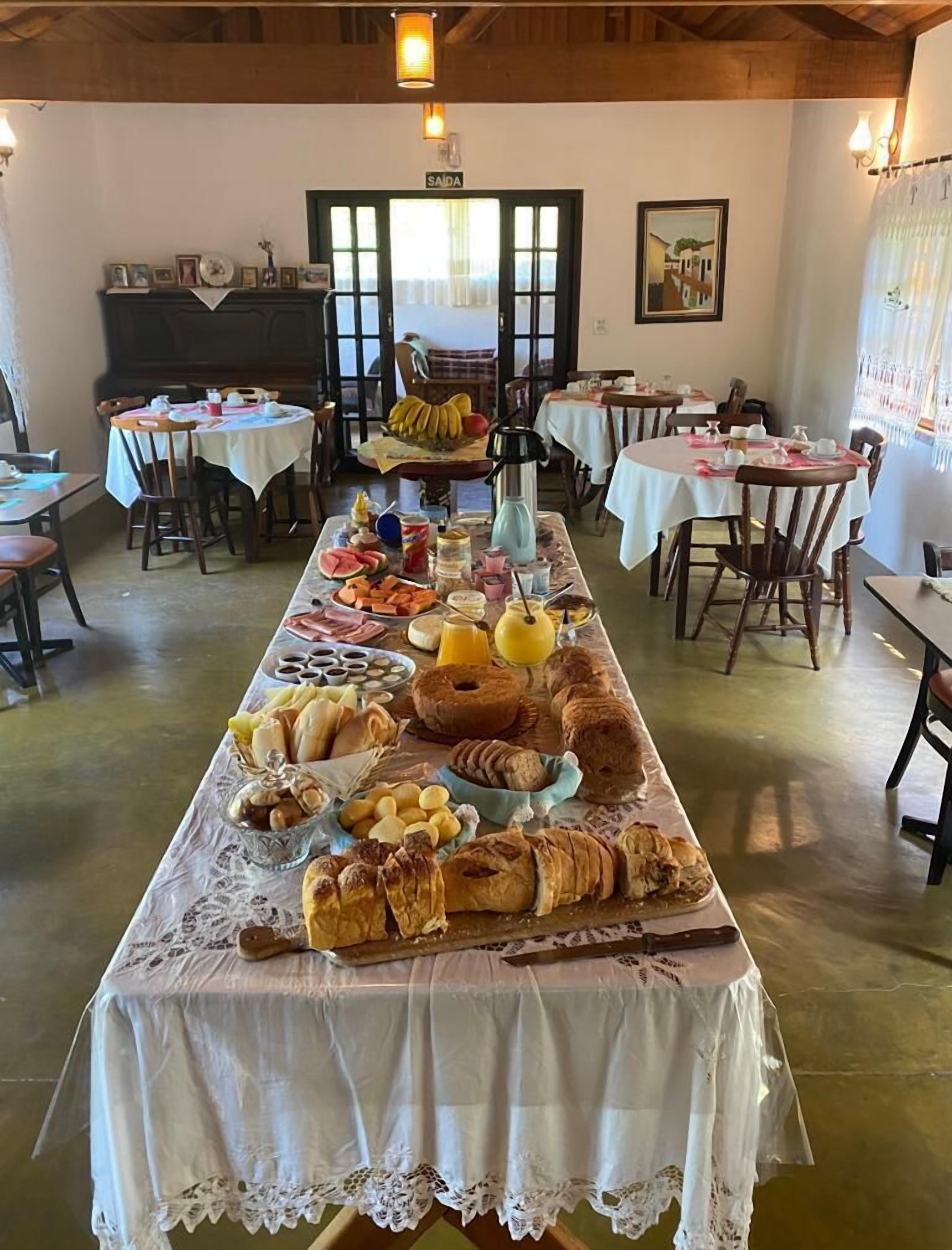 En frukostbuffé med ett urval av bakverk, frukter och drycker, uppdukad på ett långt bord i en matsal med flera bord och stolar.