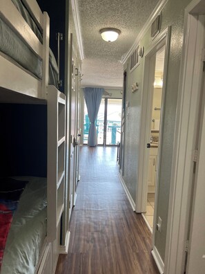 A narrow hallway with bunk beds on one side and a bathroom on the other. - Beautiful Galveston, ocean front, Ocean views, Comfortable Beds N Amazing pools. (Galveston)