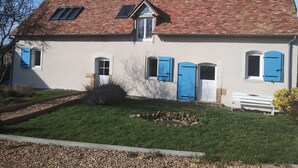 Una casa de dos pisos con techo de tejas rojas, paredes blancas y contraventanas azules.