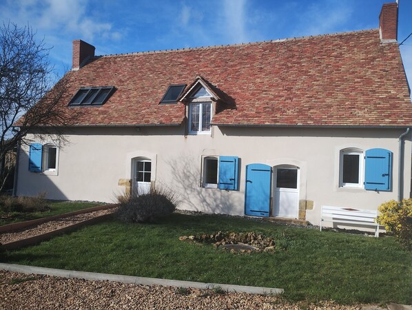 A two-story house with a red-tiled roof, white walls, and blue shutters.