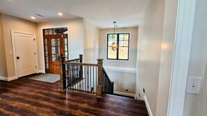 A spacious room with hardwood flooring, a wooden staircase, and a large window with a view. - Norris Lakefront Retreat—Family Ready, Private Dock, Fire Pit, Screened Porch (LaFollette)