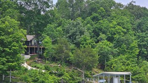 A lakeside property with a house, dock, and covered boat storage. - Norris Lakefront Retreat—Family Ready, Private Dock, Fire Pit, Screened Porch (LaFollette)