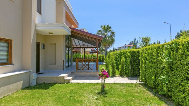 A modern building with a covered entrance, a well-maintained lawn, and a tall hedge. - Paradise Town Villa Beliza (Serik)
