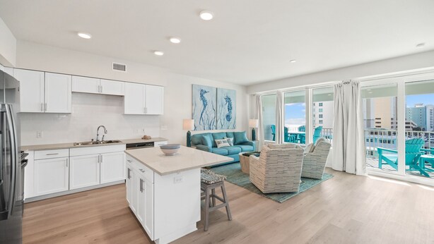 Een moderne keuken met witte kasten, een centraal eiland en een eethoek met turquoise stoelen.
