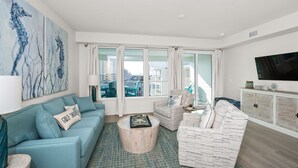 Een moderne woonkamer met een blauwgroene bank, een ronde salontafel en een groot schilderij van een zeepaard aan de muur.