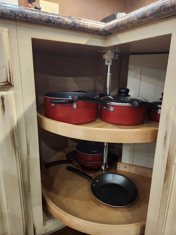A kitchen with wooden shelves holding red pots and pans.