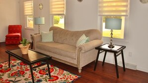 A living room with a beige sofa, two side tables, a red armchair, and a patterned rug. - Cozy Matthews House in a Convenient Location (Matthews)