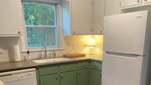 A kitchen with green cabinets, a white refrigerator, a wooden countertop, a sink, and a window with a view of trees. - Cozy Matthews House in a Convenient Location (Matthews)