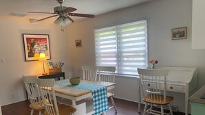 A dining area with a table set for four, white chairs, a ceiling fan, and a window with blinds. - Cozy Matthews House in a Convenient Location (Matthews)