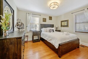 Cozy bedroom with a large bed, dresser, and nightstand, featuring a ceiling light fixture and two windows with blinds.