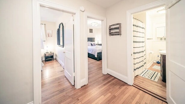 Un pasillo con piso de madera que conduce a un dormitorio con cama y mesita de noche.