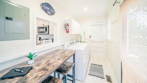 Cocina compacta con una mesa de madera, microondas y un letrero de lavandería autoservicio.