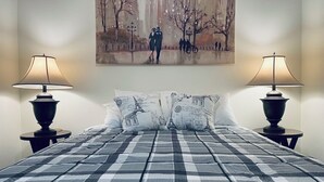 Una cama con colcha a cuadros, dos lámparas de noche y dos almohadas con estampado de París.