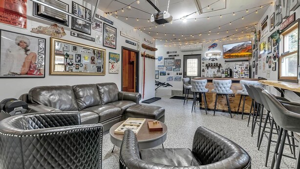 Un rincón de sala cómodo con un sofá de cuero, una mesita redonda y una zona de bar con taburetes.