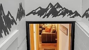 Una escalera conduce a una habitación con un adhesivo mural con motivos de montaña, un letrero de bienvenida y una alfombra marrón.
