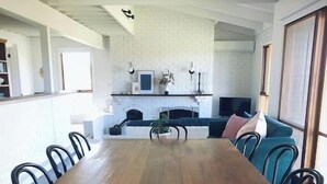 En rummelig spiseplads med et langt træbord og sorte stole, en pejs og et hyggeligt siddeområde med sofa og stole.
