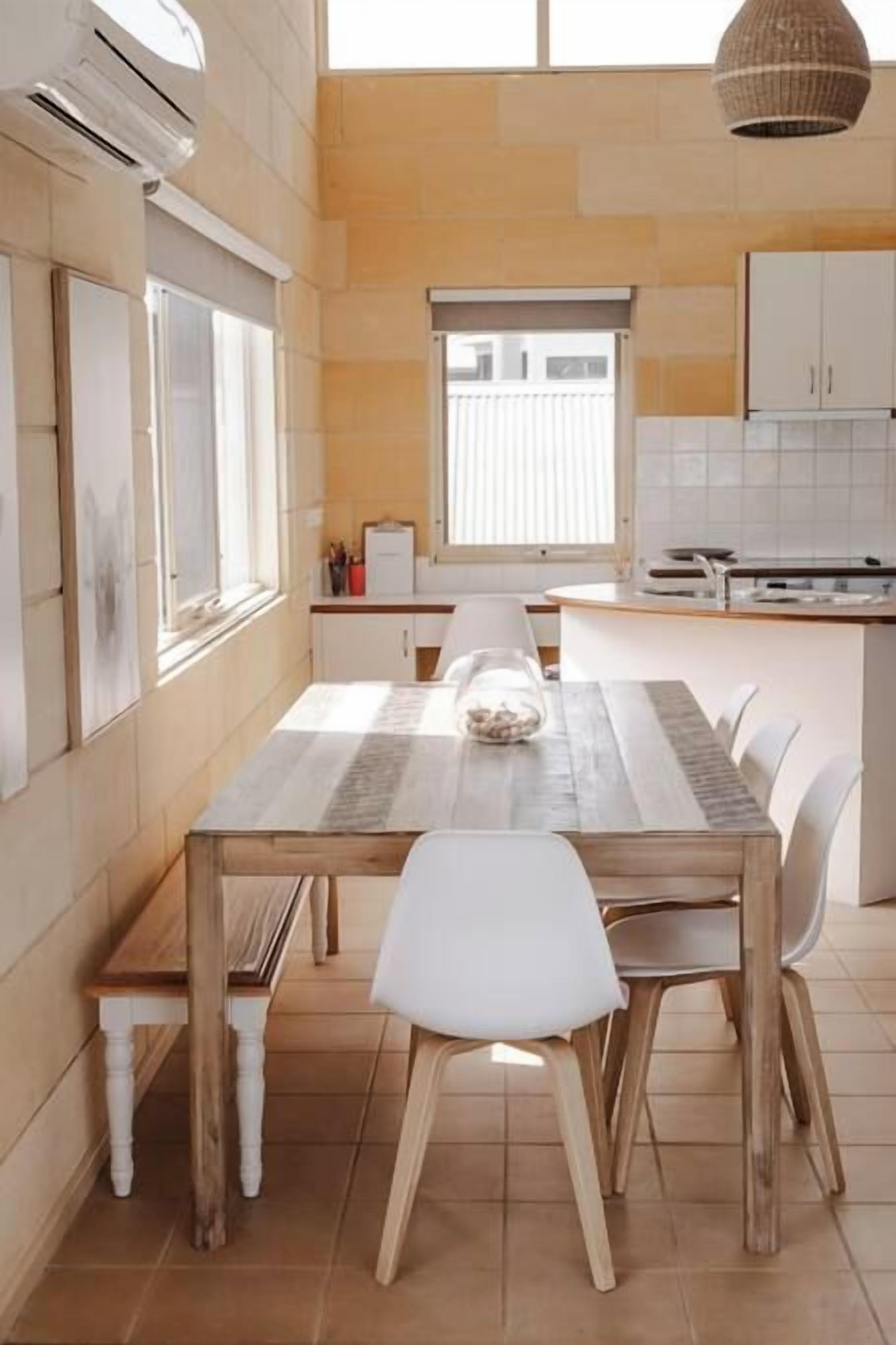 Une cuisine moderne avec une table à manger en bois, des chaises blanches et une fenêtre qui laisse entrer la lumière naturelle.
