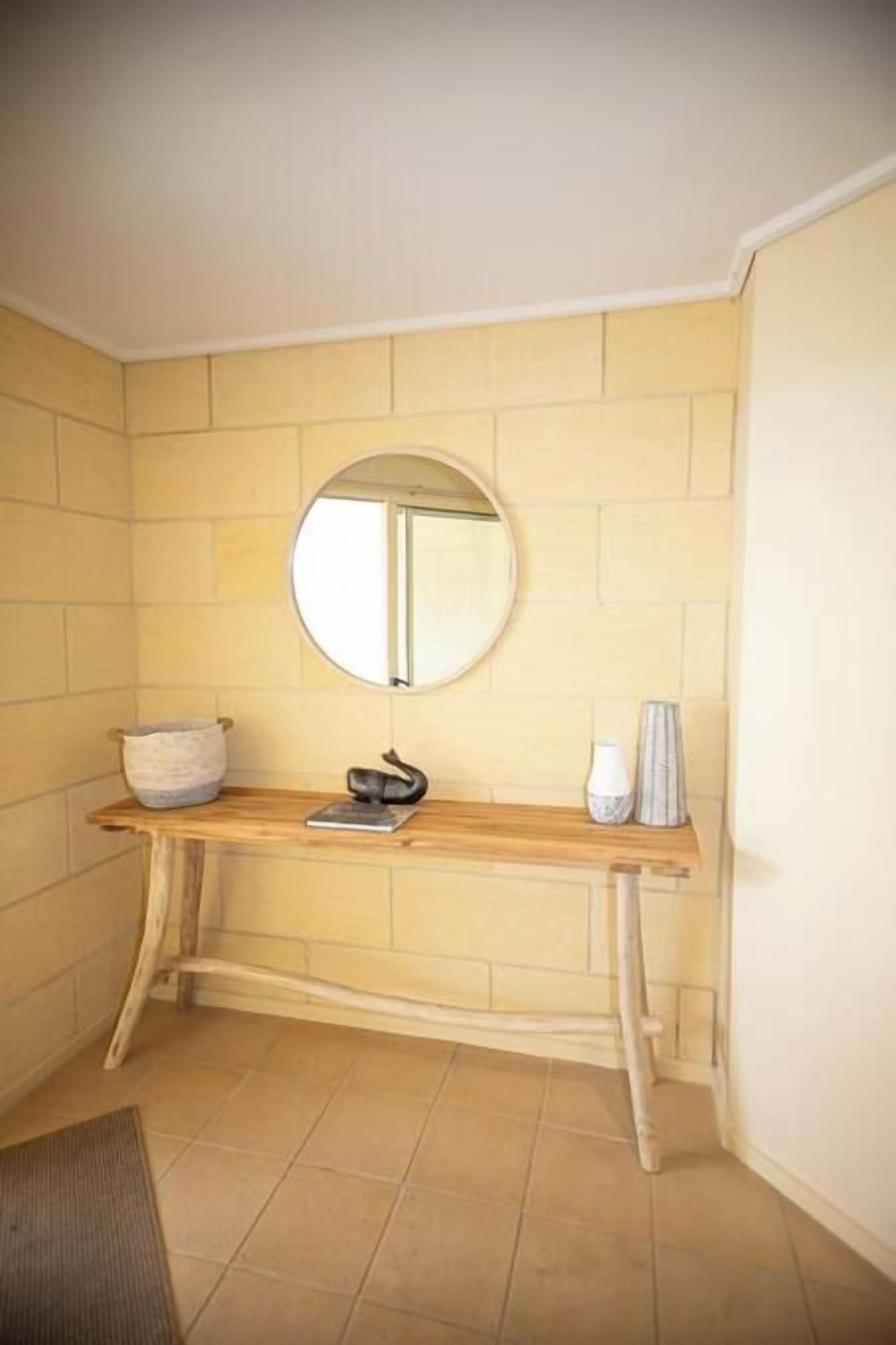 A bathroom with a wooden vanity, a round mirror, and a towel rack.