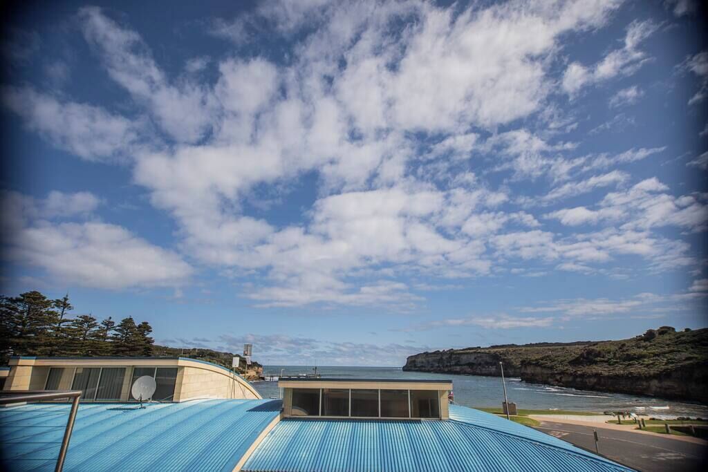 Ein Küstenhotel mit blauem Dach, Blick auf das Meer und einer Klippe im Hintergrund.