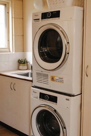 A stacked washer and dryer unit in a kitchen with a window and a sink. - Surf break - Beachfront Port Campbell (Port Campbell)