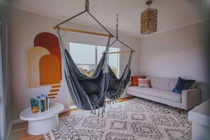 Un soggiorno moderno con un'amaca sospesa, un divano bianco, un tappeto decorato e un design minimalista delle pareti.