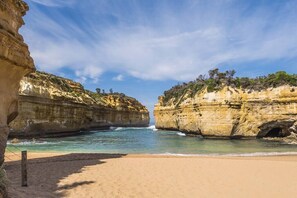 A beach with clear blue water, sandy shore, and rocky cliffs.