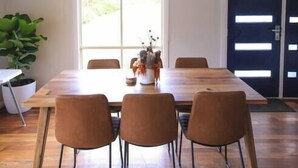A dining area with a wooden table and four chairs, a potted plant, and a window with blinds. - The Hangout KING BEDS Hammock Chairs with a View (Port Campbell)