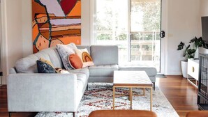 A living room with a grey sofa, a coffee table, and a colorful abstract painting. - The Hangout KING BEDS Hammock Chairs with a View (Port Campbell)
