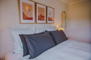 A bed with a striped bedspread, multiple pillows, and three framed artworks on the wall above.