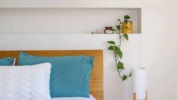 A bed with a wooden headboard, a bedside table with a lamp, and a shelf with a plant.