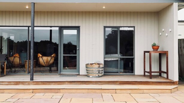 Una casa moderna con un patio cubierto que cuenta con puertas de vidrio correderas, una mesa de madera y una planta en maceta.