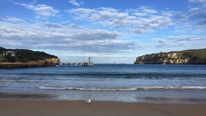 Una playa con un muelle que se adentra en aguas tranquilas, rodeada de acantilados.