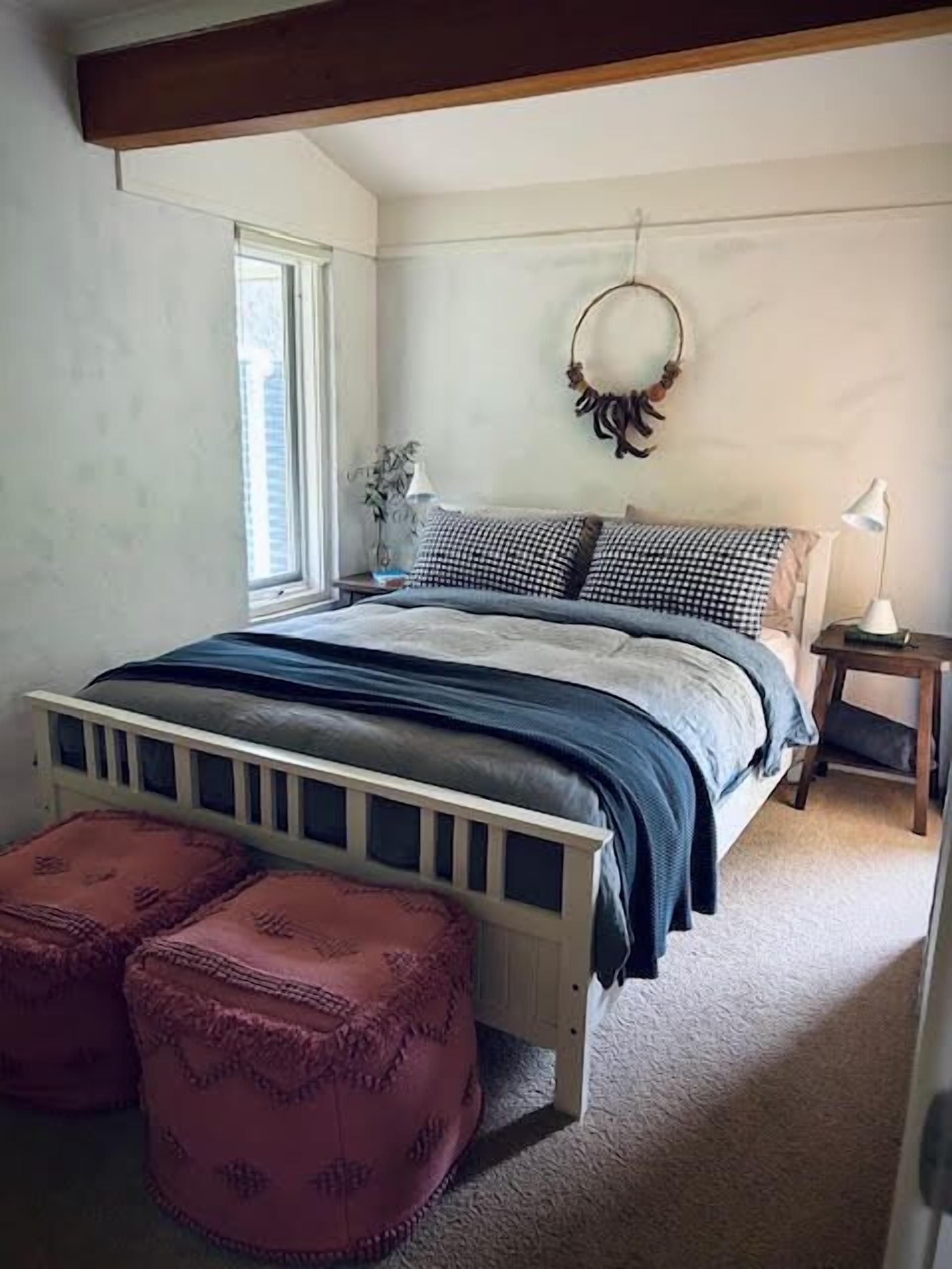 Een slaapkamer met een bed, twee nachtkastjes, een raam en een spiegel aan de muur.
