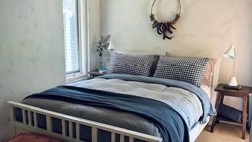 Een slaapkamer met een bed, twee nachtkastjes, een raam en een spiegel aan de muur.