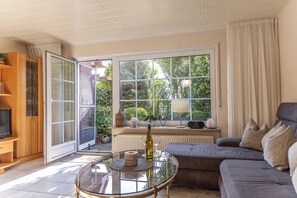 A living room with a sofa, a glass coffee table, a TV, and a large window with curtains. - Ferienhaus 50084 - Platz und Behaglichkeit Satt: In dem Reihenhaus von ca. 100 qm Sorgen der (Wittmund)
