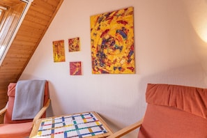 Una stanza accogliente con travi a vista, una sedia di legno con un asciugamano grigio, un divano rosso e un tavolino trapuntato.