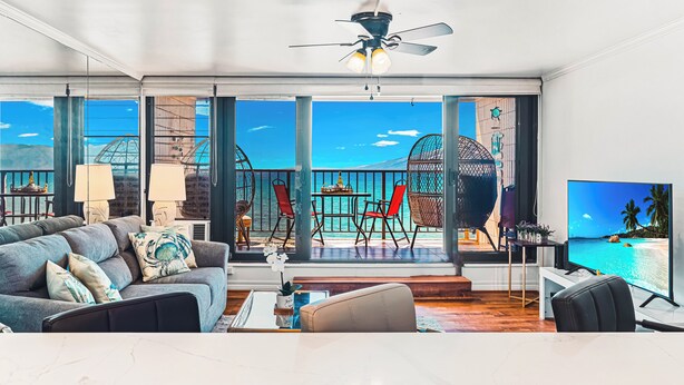 Un salon moderne doté d’un grand téléviseur, de sièges confortables et d’un balcon offrant une vue sur la mer.