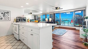 Une cuisine moderne avec des meubles blancs, un grand îlot central et une vue sur le balcon.
