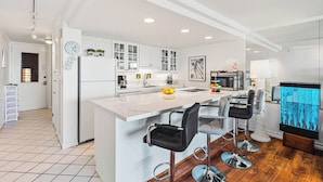 Une cuisine moderne avec des meubles blancs, un îlot central doté de tabourets, un réfrigérateur et un four à micro-ondes.