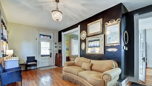 A living room with a beige sofa, wooden flooring, a chandelier, and wall-mounted decorations. - Historic Talbott Street Home-Hot Tub and Fire Pit! (Indianapolis)