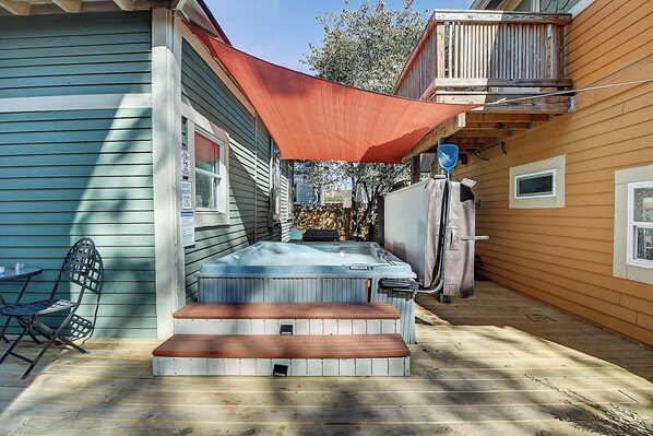 Un patio trasero con jacuzzi, terraza de madera y zona de patio cubierta.
