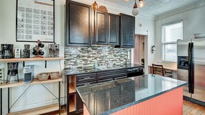 A modern kitchen with dark cabinets, a large island, and a barista chart on the wall. - Historic Talbott Street Home-Hot Tub and Fire Pit! (Indianapolis)