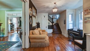 A spacious living room with hardwood floors, a beige sofa, a piano, and a chandelier. - Historic Talbott Street Home-Hot Tub and Fire Pit! (Indianapolis)