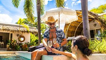 A man and a woman sitting by a poolside, holding wine glasses.