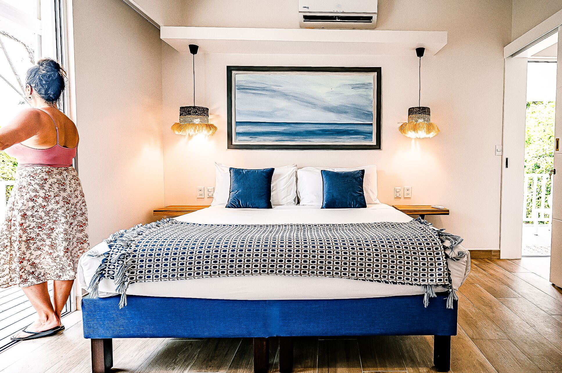 Une chambre à coucher avec un lit, deux tables de chevet, un tableau au mur et deux lampes suspendues.