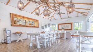 Un comedor con mobiliario blanco, suelo de madera y vigas en el techo.