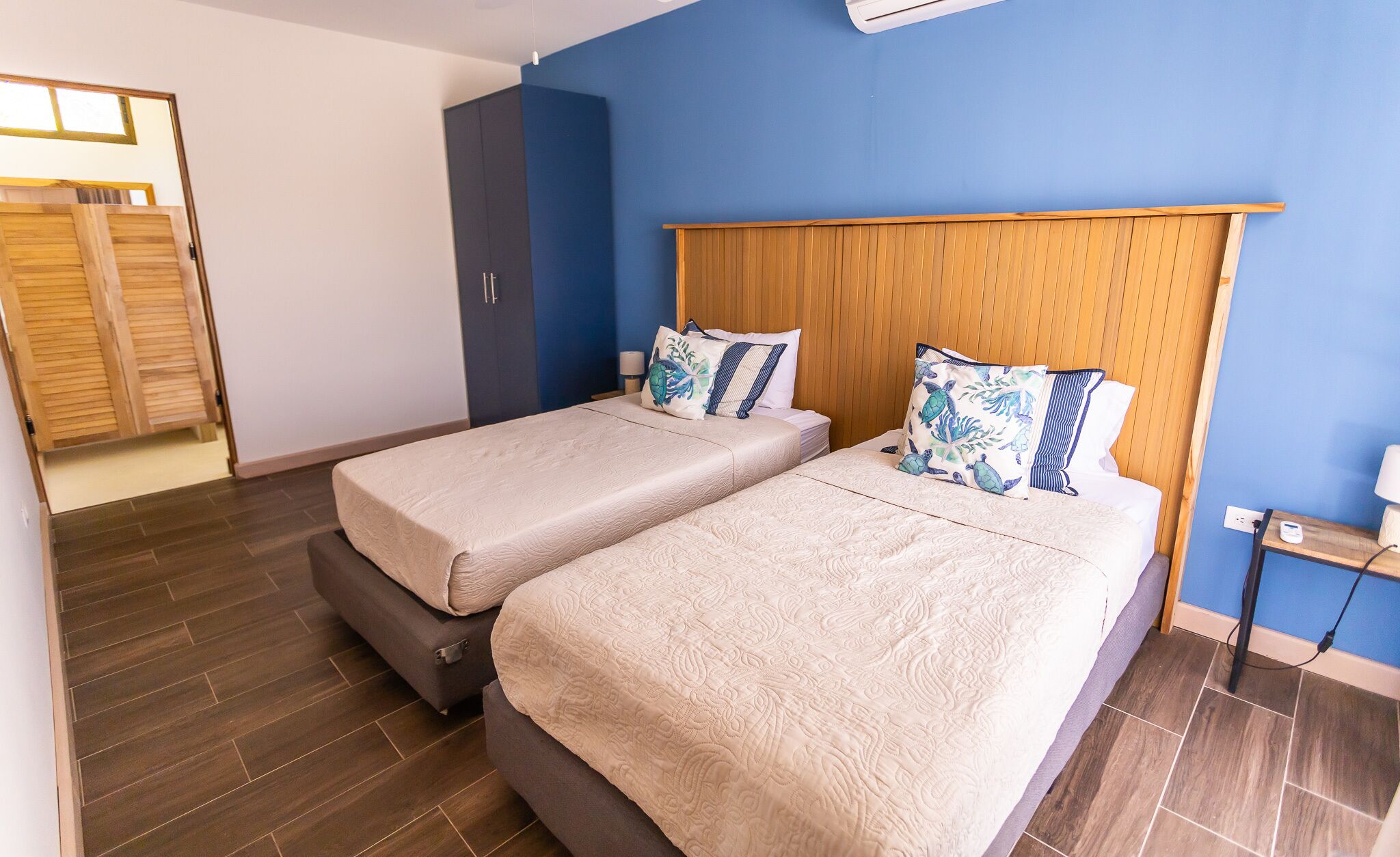 A double room with two beds, a wooden wardrobe, a nightstand, and a bathroom door.