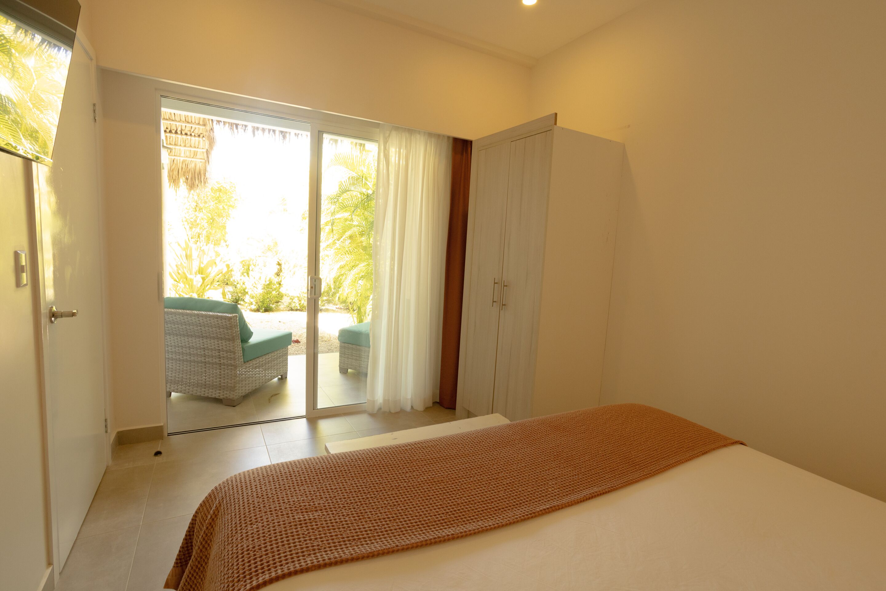 Quarto com cama, guarda-roupa e porta de vidro deslizante para área externa com cadeira e mesa.