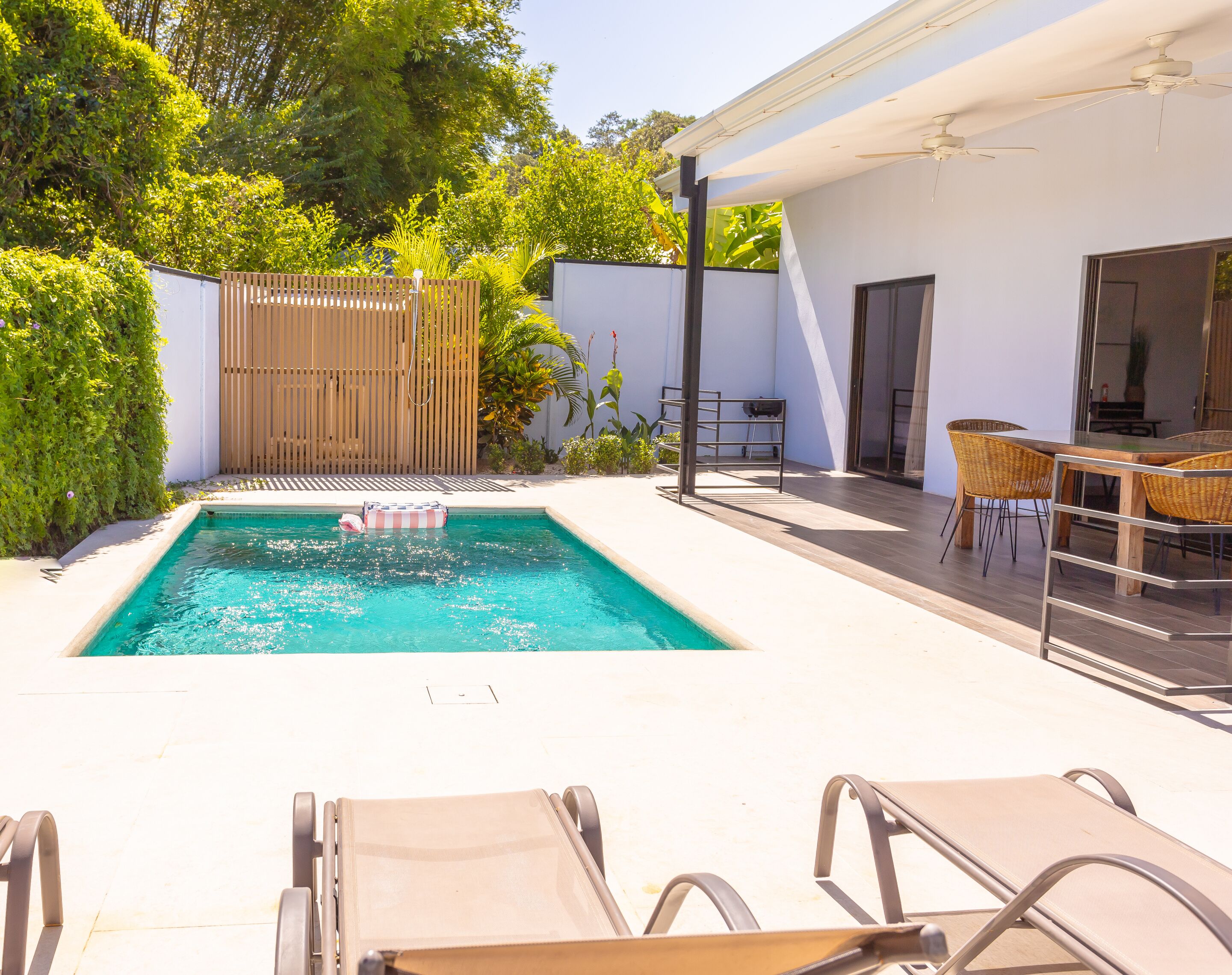 A swimming pool with lounge chairs, a wooden fence, and a table with chairs.