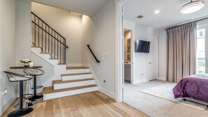 Un intérieur moderne avec un escalier, un téléviseur à écran plat, un lit recouvert d’une courtepointe violette et une petite table ronde sur laquelle est posée une bougie.